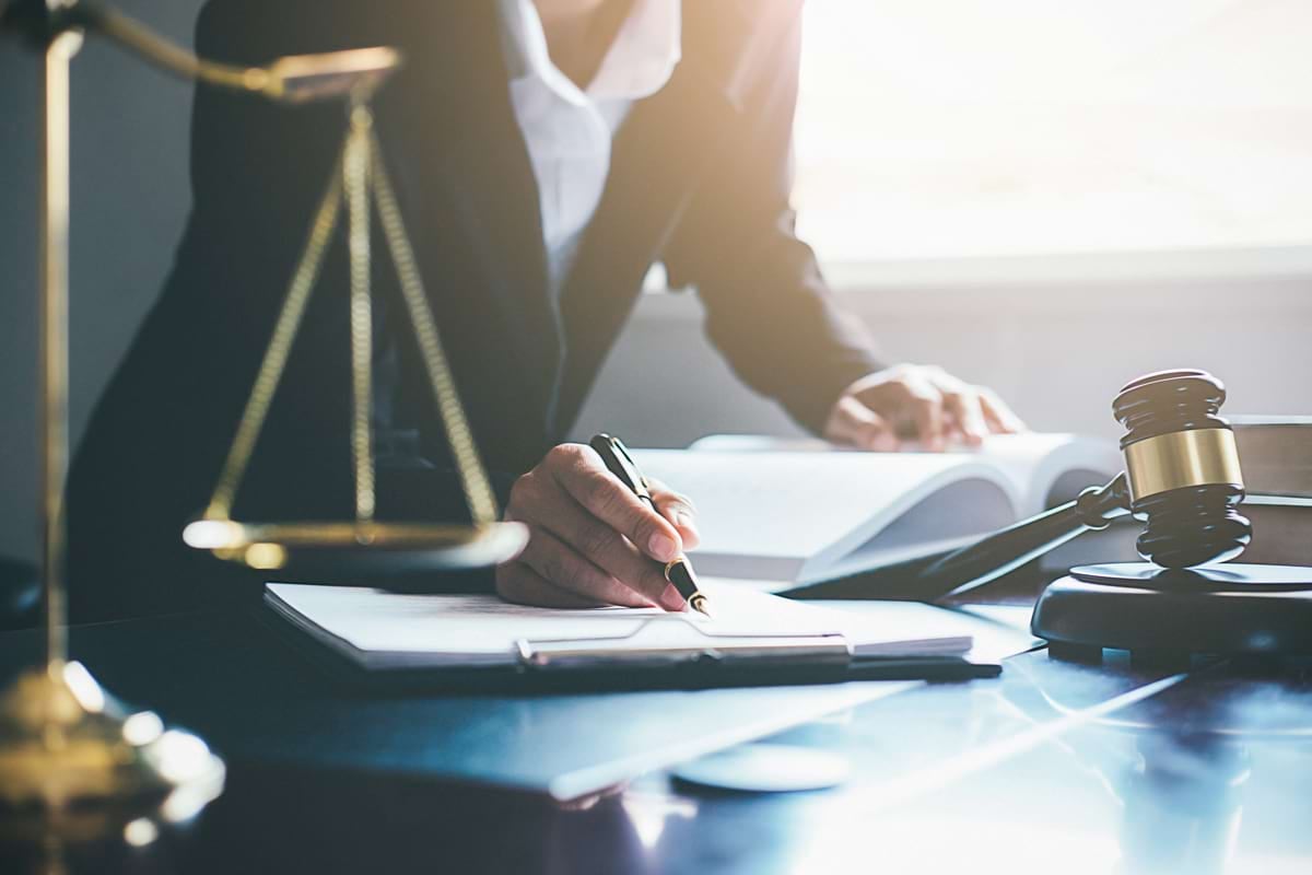 A lawyer at a desk writing, with a scale of justice and a gavel nearby.