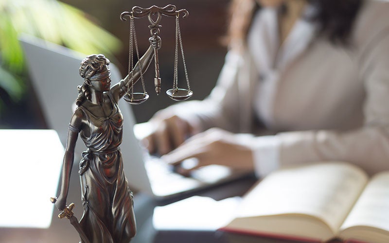 Bronze statue of Lady Justice with scales, with a person on a laptop