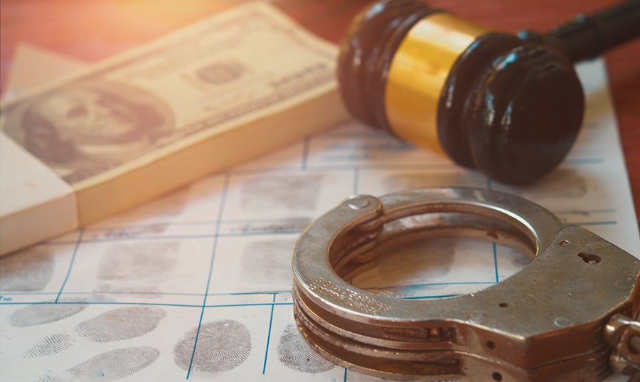 Handcuffs, gavel, and a stack of money on a fingerprint card, symbolizing crime, justice, and bribery.