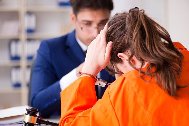 Stressed, handcuffed person in an orange jumpsuit consulting with a lawyer.