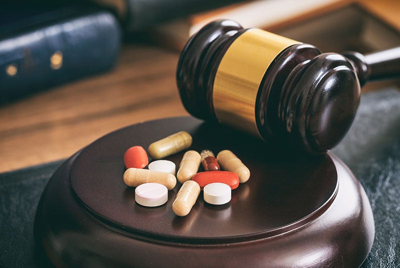 A wooden gavel with a golden band rests next to a pile of multi-colored pills on its base.