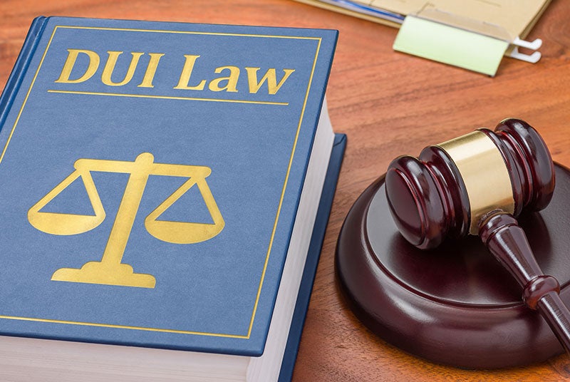 A blue book titled DUI Law with scales of justice on the cover, next to a wooden gavel.