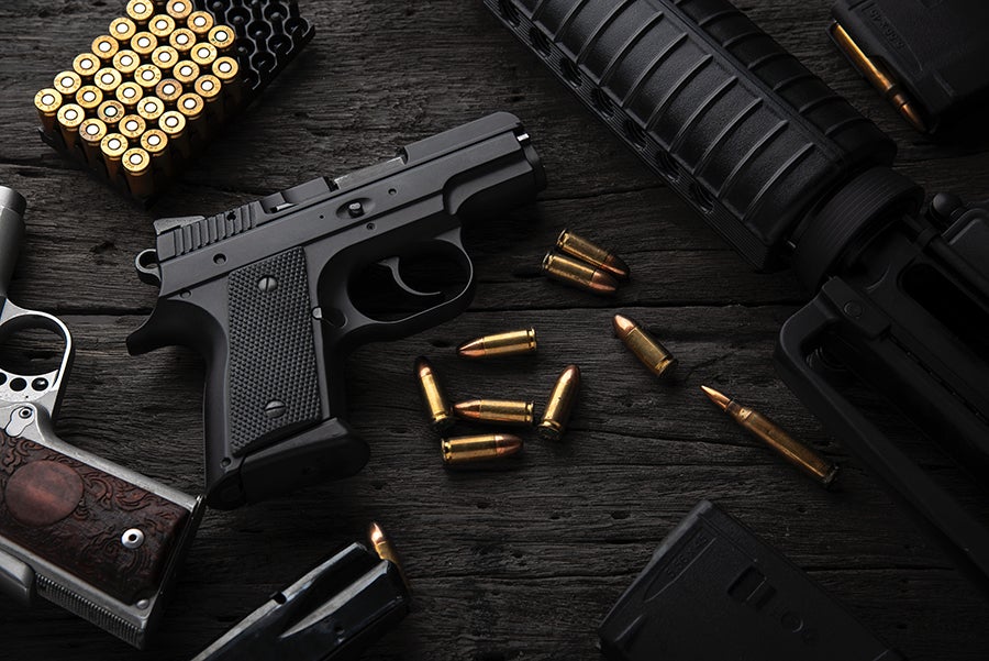 Various firearms and ammunition, including two pistols and a rifle, displayed on a dark wooden surface.