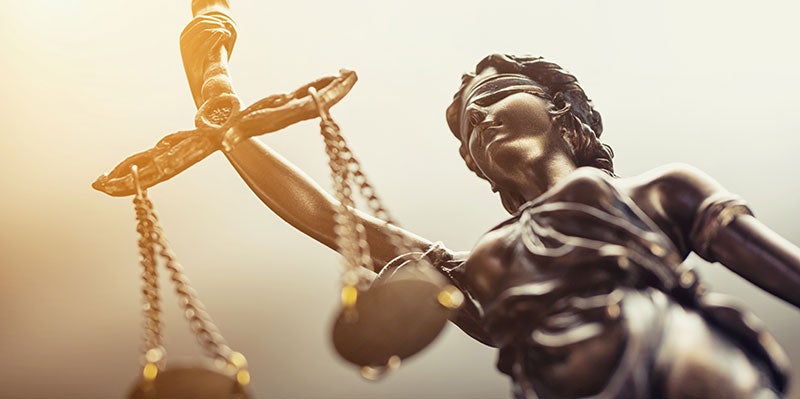 A bronze statue of Lady Justice, blindfolded and holding scales, with a bright light shining from the upper left.