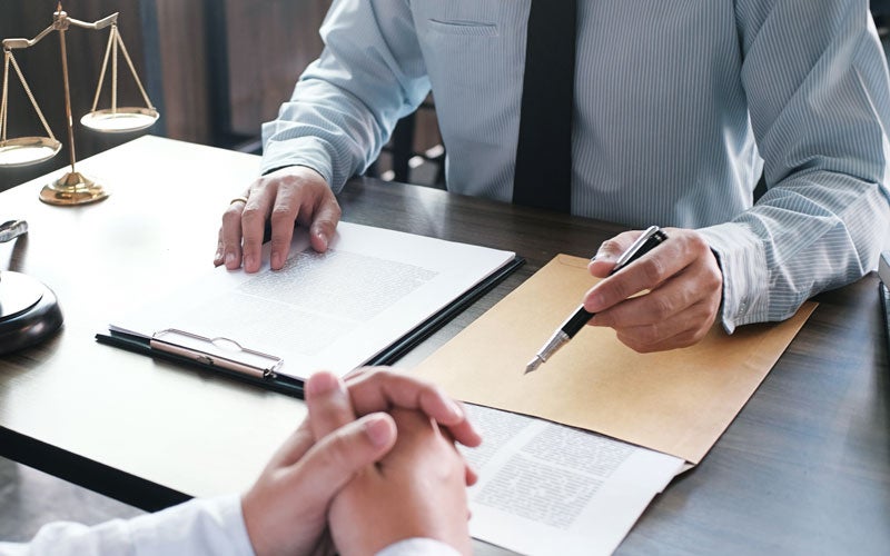 A lawyer in a striped shirt and tie gestures with a fountain pen while discussing documents with a client.