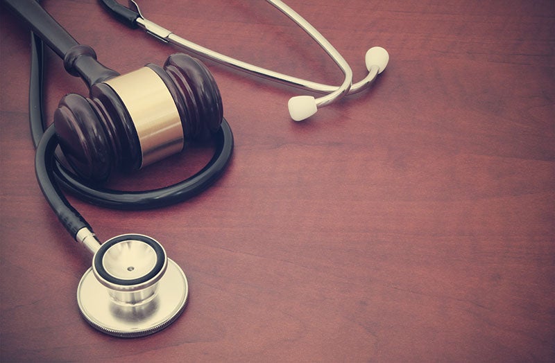 A wooden gavel rests on a stethoscope on a wooden table.