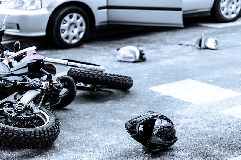 A motorcycle lies on the asphalt after a collision with a car, with a helmet and debris scattered nearby.