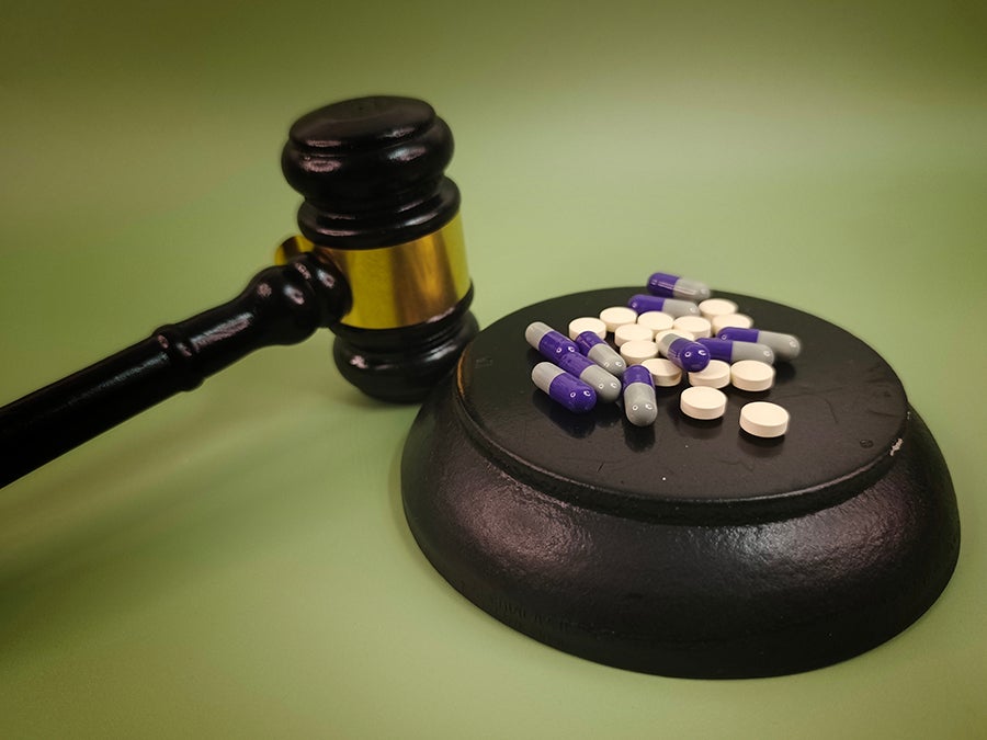 A judge's gavel beside white pills and purple and grey capsules on a black base.
