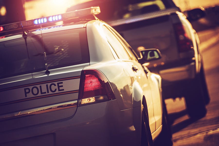 Rear view of a white police car with flashing blue lights and POLICE written on the trunk.
